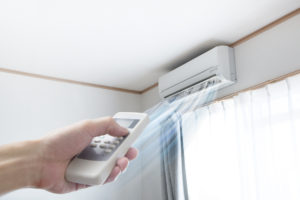 ductless mini-split on wall with air flow and a hand pointing a remote at the system